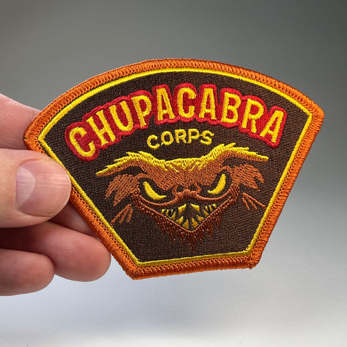 Hand holding the Chupacabra Corps cryptid military badge embroidered patch