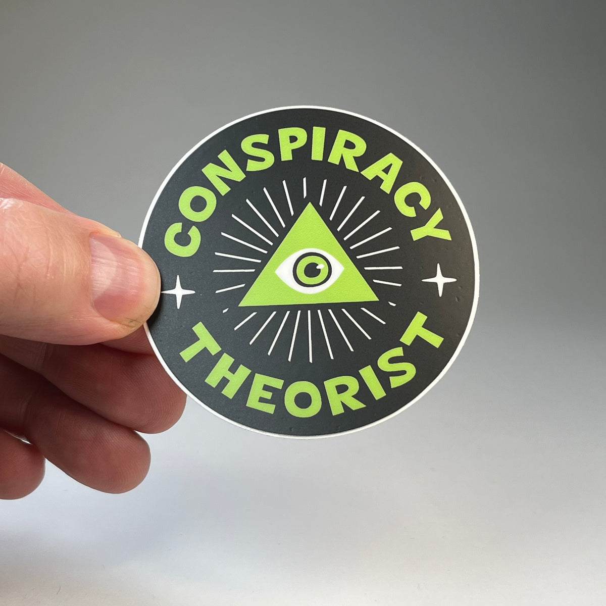 Hand holding the Conspiracy Theorist circle sticker