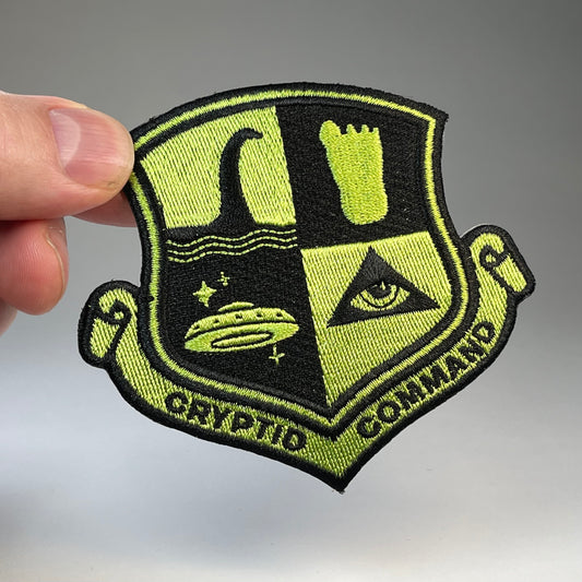 Hand holding the Cryptid Command military badge embroidered patch