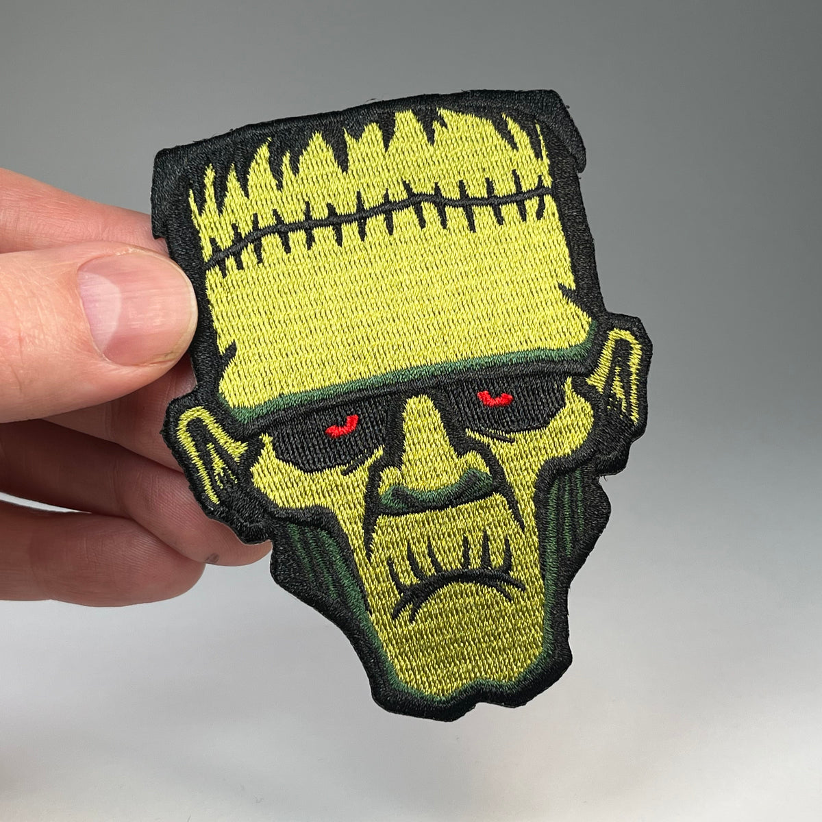 Hand holding the Frankenstein Monster head embroidered patch
