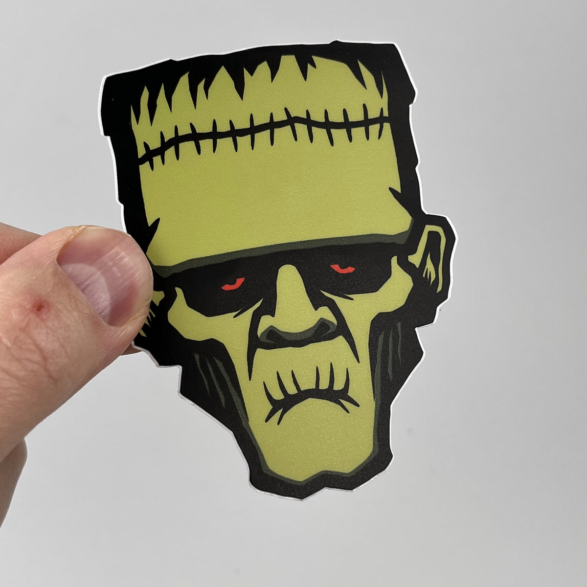 Hand holding the Frankenstein Monster horror sticker, green Frankenstein head