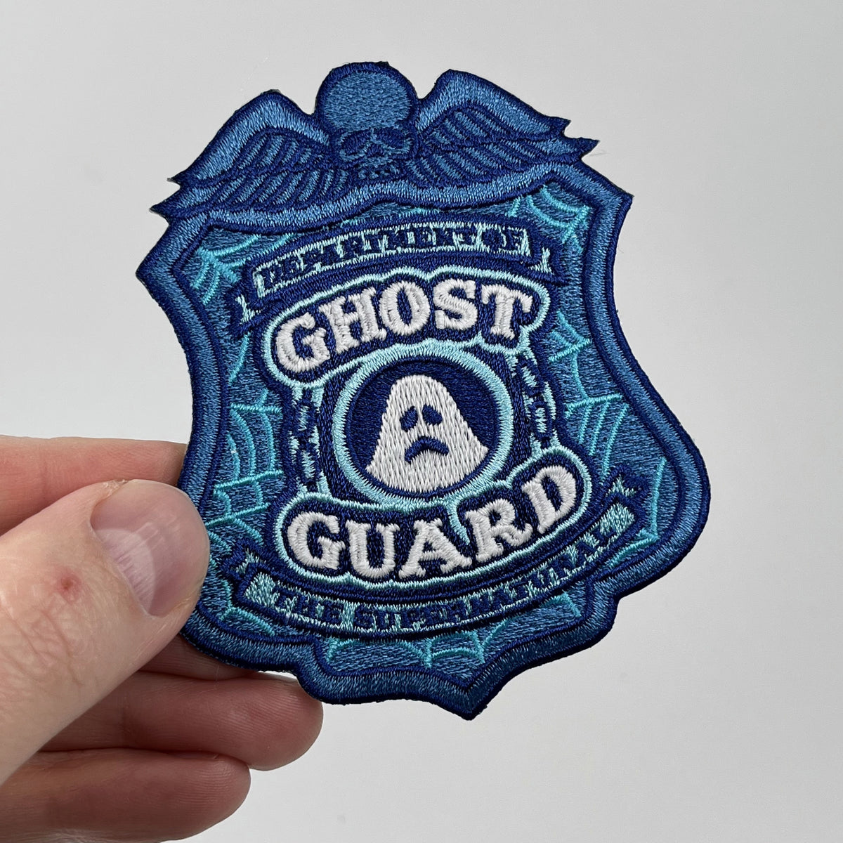 Hand holding the Ghost Guard police badge embroidered patch, blue shield with a ghost