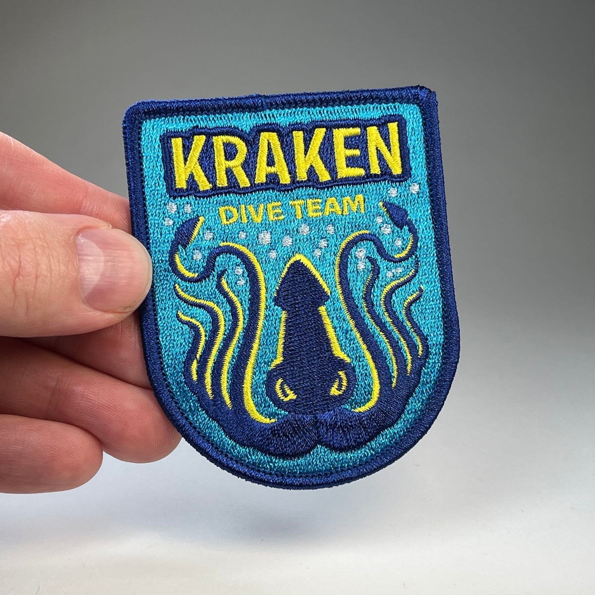 Hand holding the Kraken Dive Team cryptid military badge embroidered patch