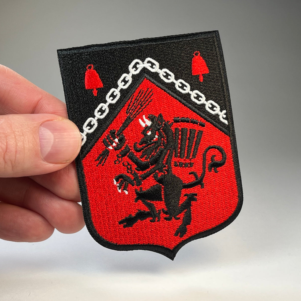 Hand holding the Krampus Rampant medieval heraldic shield embroidered patch