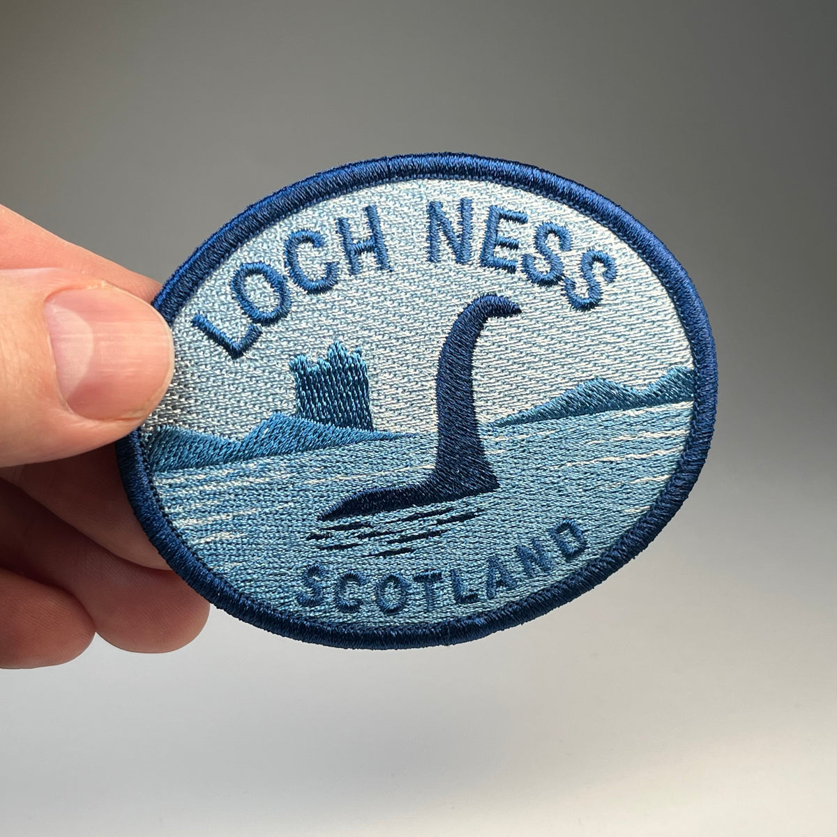 Hand holding the Loch Ness Scotland Nessie cryptid travel patch