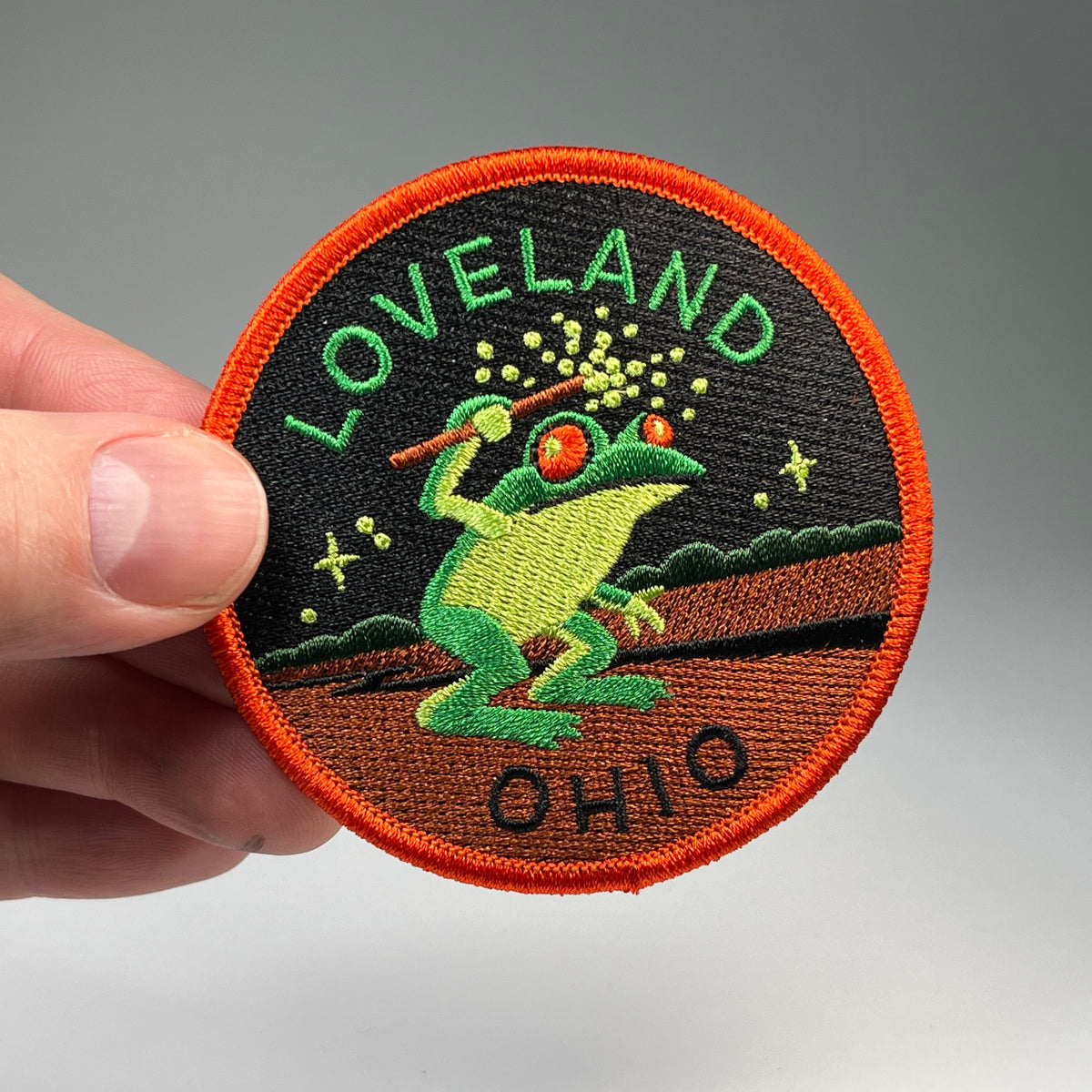Hand holding the Loveland Ohio Frogman cryptid travel patch