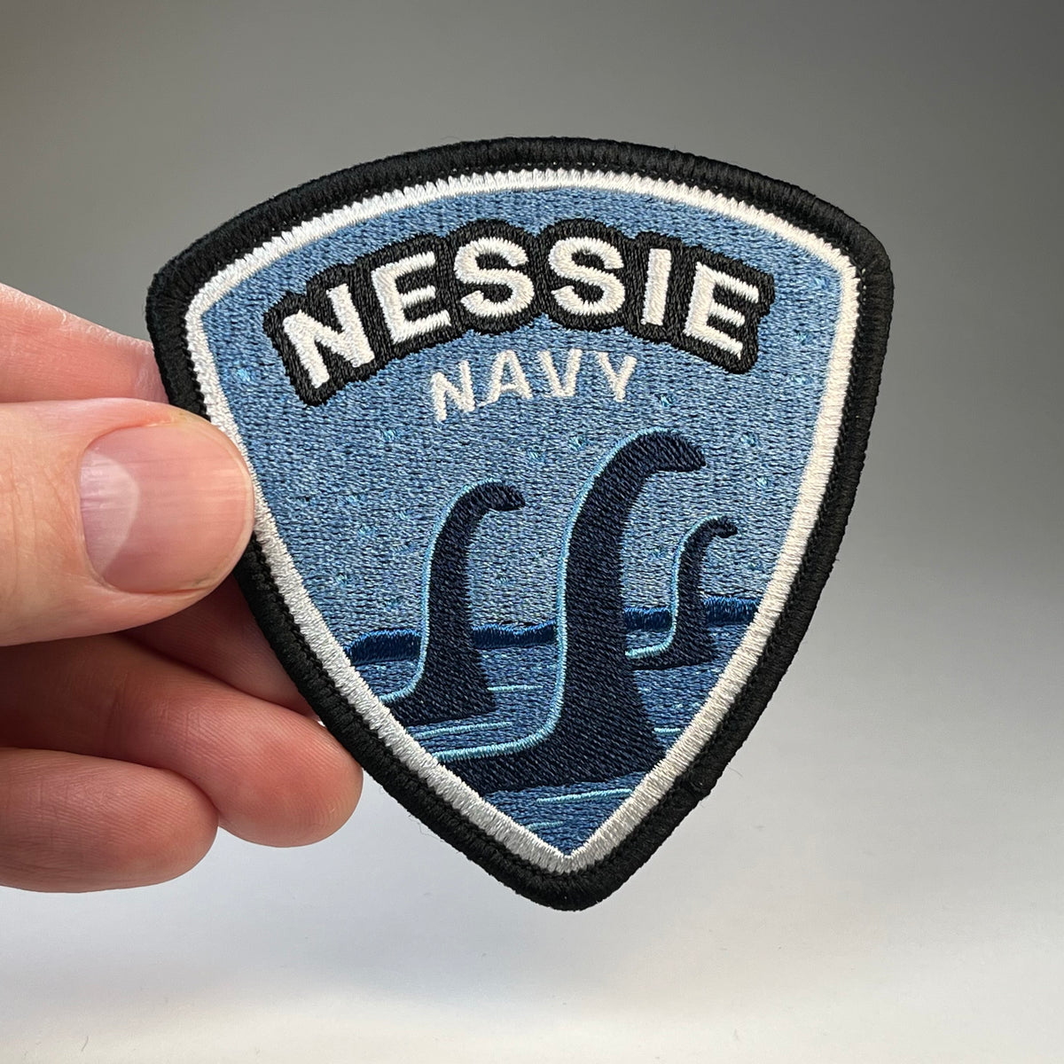 Hand holding the Nessie Navy cryptid military badge embroidered patch