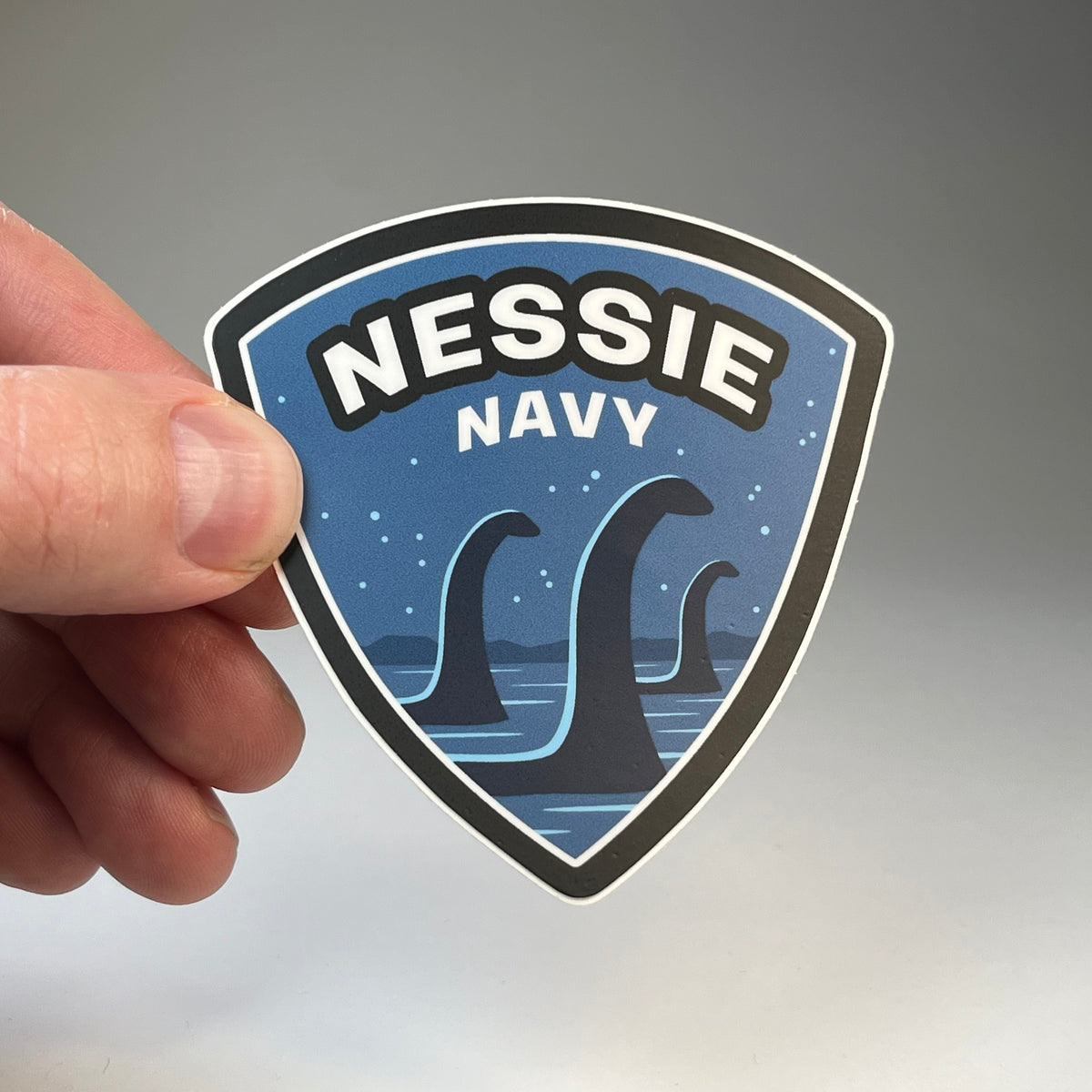 Hand holding the Nessie Navy cryptid military badge sticker
