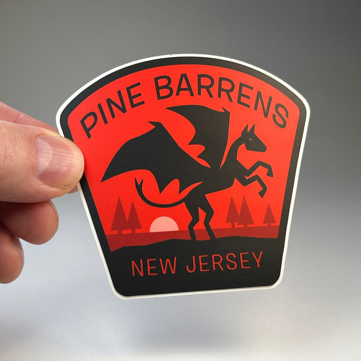 Hand holding the Pine Barrens New Jersey Devil cryptid travel sticker