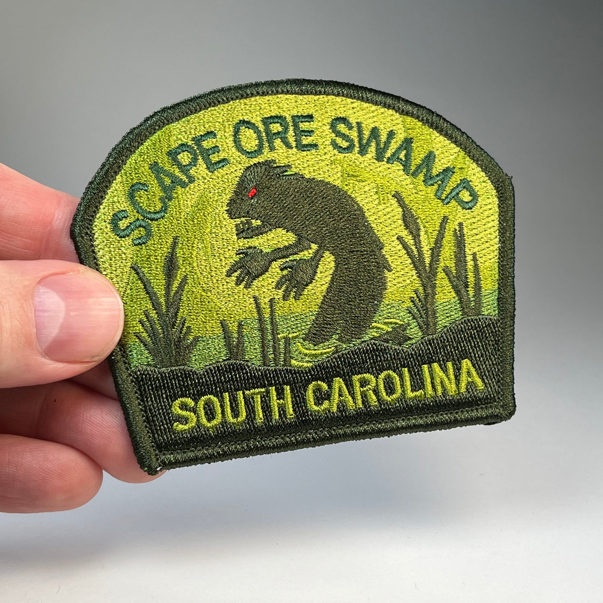 Hand holding the Scape Ore Swamp South Carolina Lizardman cryptid travel patch