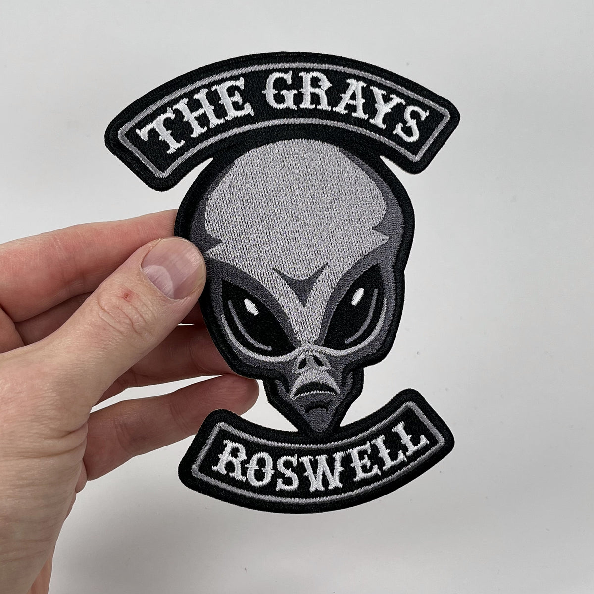 Hand holding the Grays alien embroidered patch, gray alien head with Roswell rocker banners