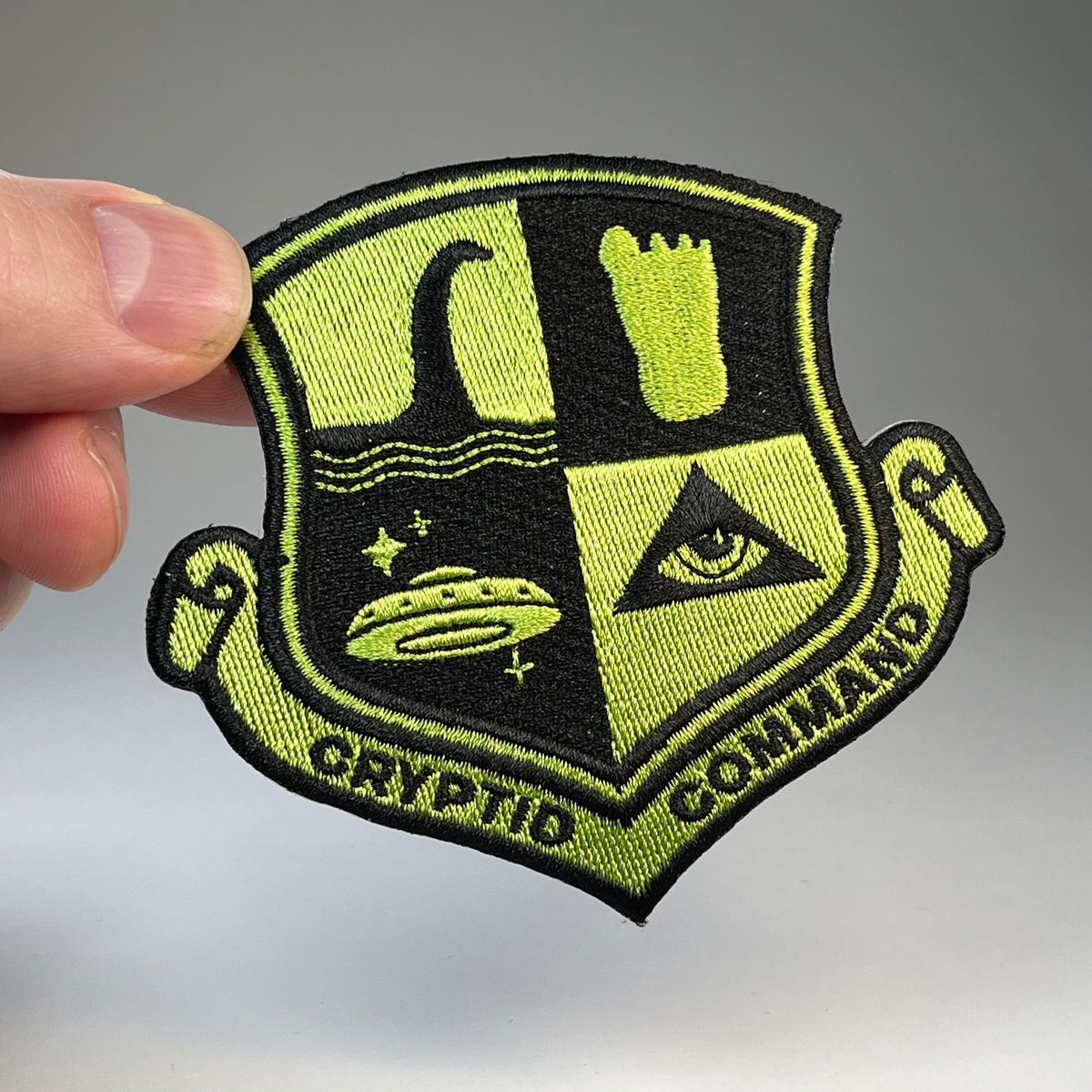 Hand holding the Cryptid Command military badge embroidered patch