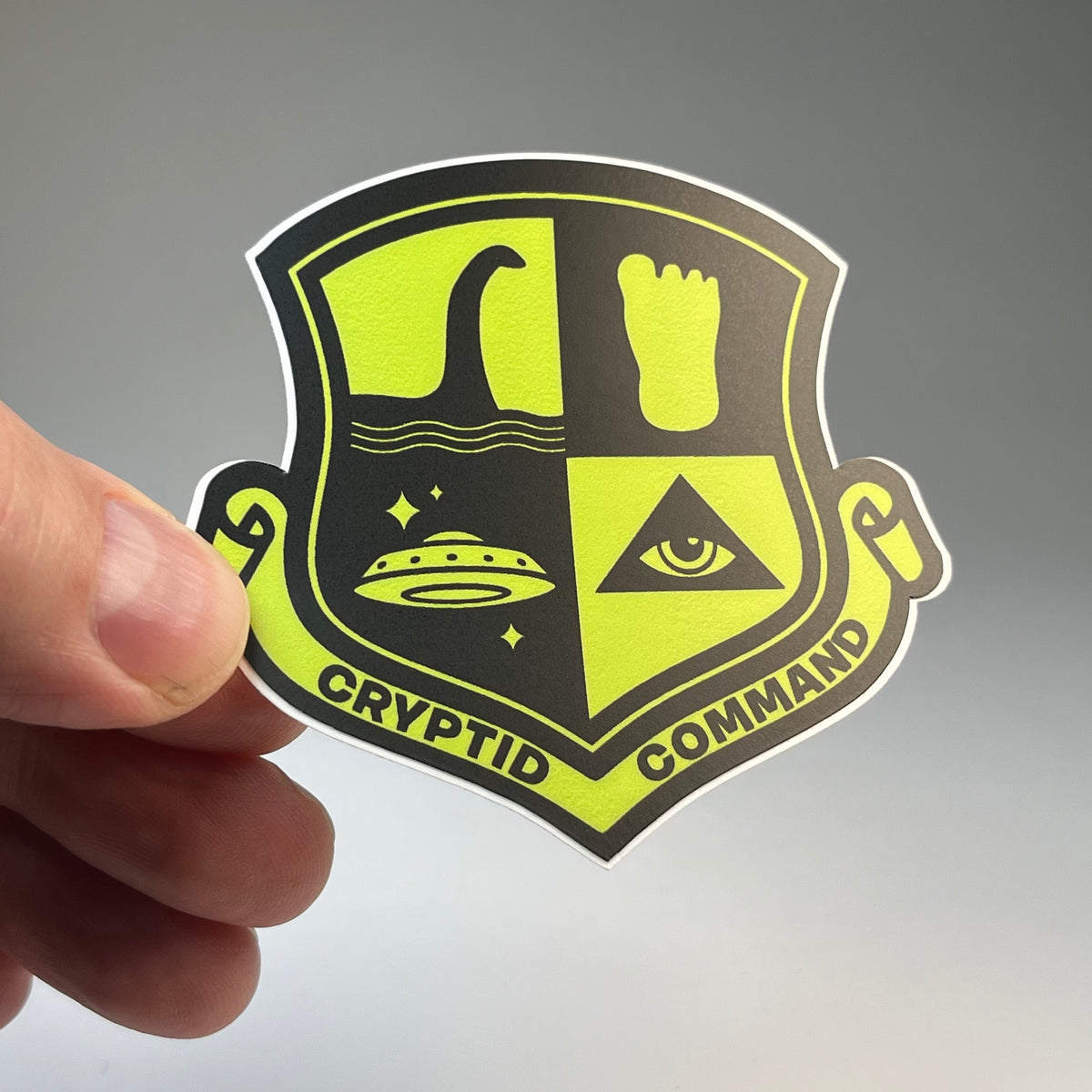 Hand holding the Cryptid Command military badge sticker