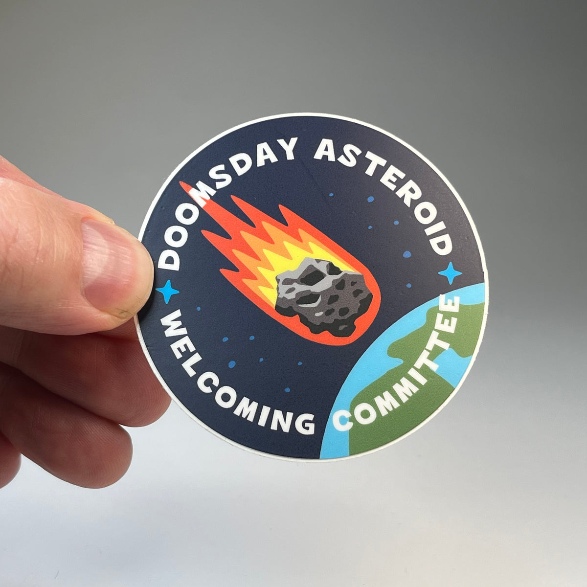 Hand holding the Doomsday Asteroid Welcoming Committee sticker