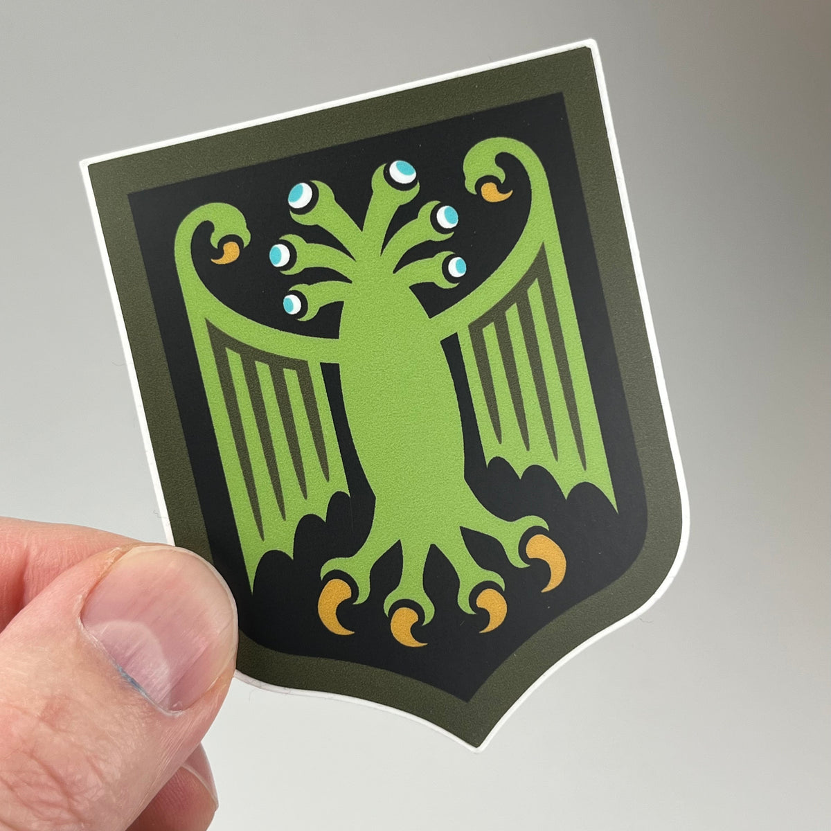 Hand holding the Elder Thing Heraldic Shield Sticker Arkham Variant