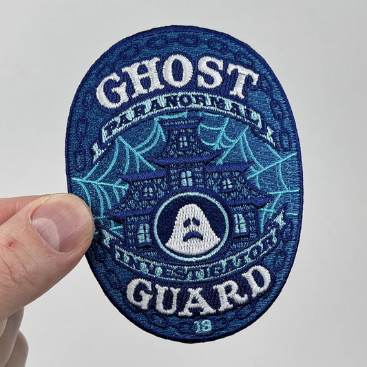 Hand holding the Ghost Guard Paranormal Investigator embroidered patch, blue oval with a haunted house and ghost