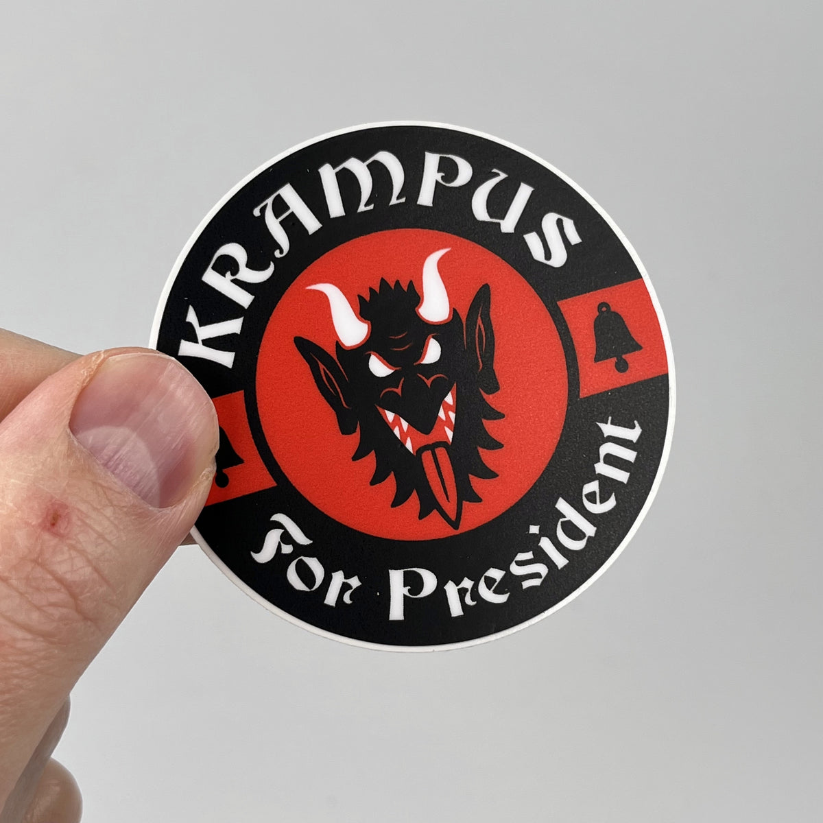 Hand holding the Krampus For President campaign sticker, black and red circle badge