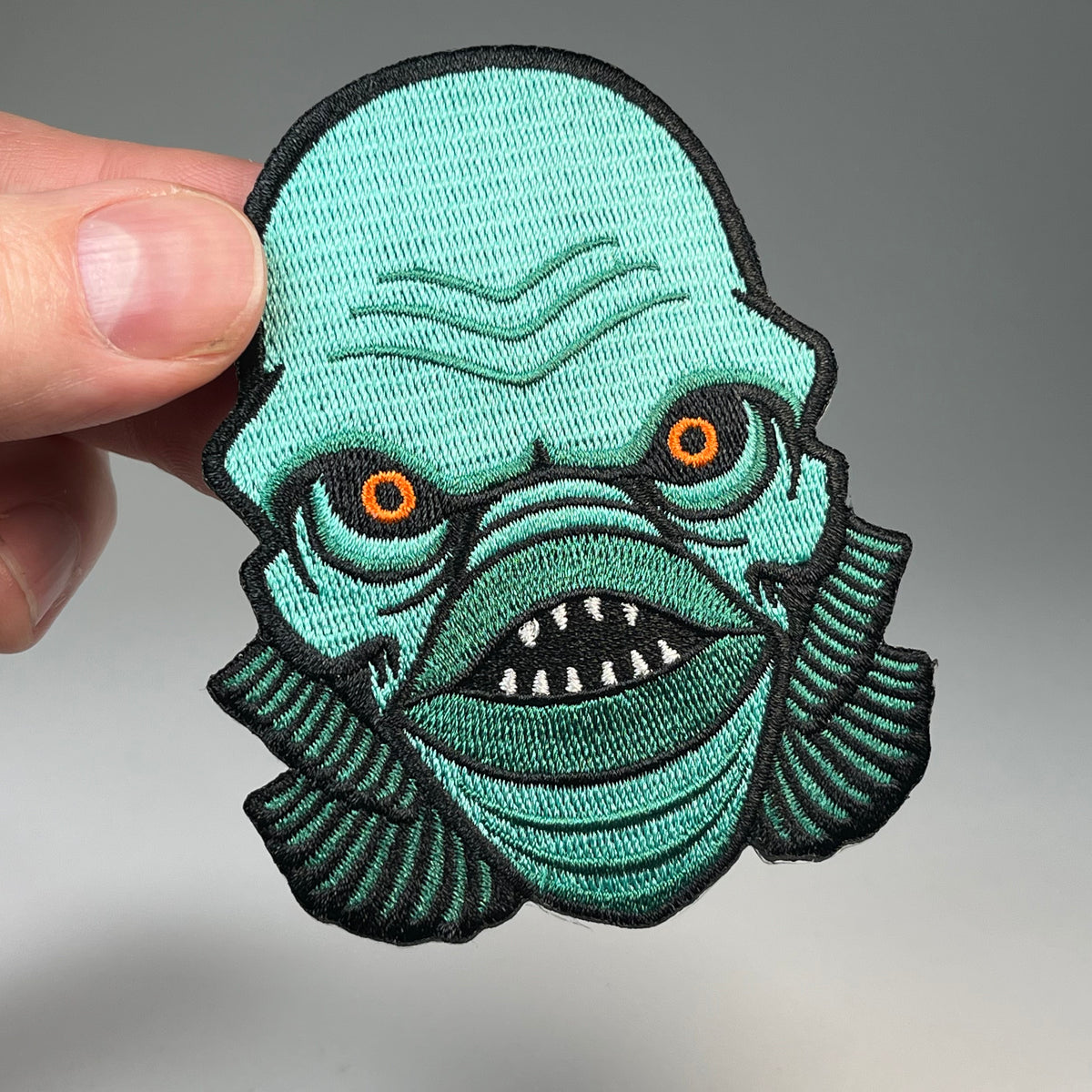 Hand holding the Lagoon Creature head embroidered patch