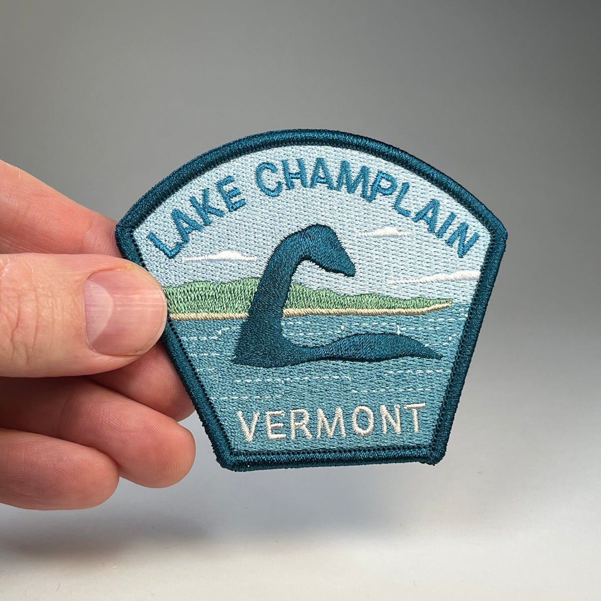 Hand holding the Lake Champlain Vermont Champ cryptid travel patch