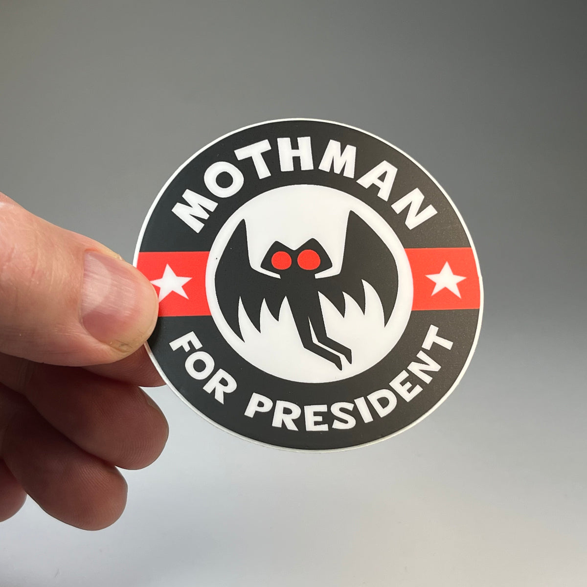 Hand holding the Mothman For President campaign cryptid sticker