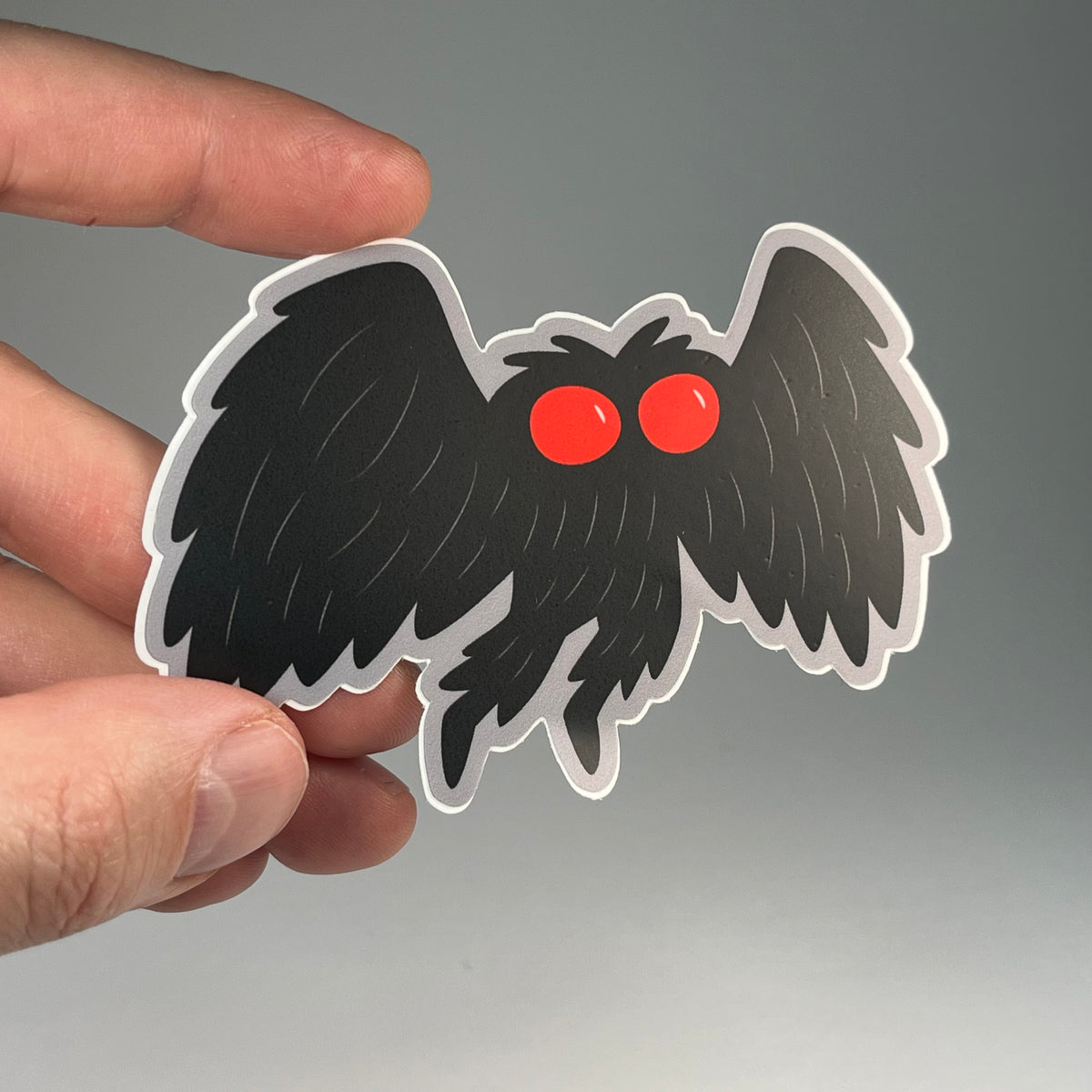 Hand holding the Mothman cute cryptid sticker
