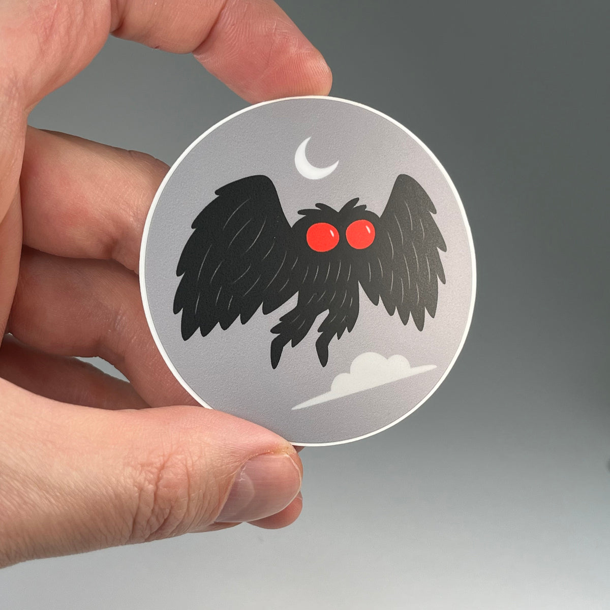 Hand holding the Mothman moon cryptid sticker