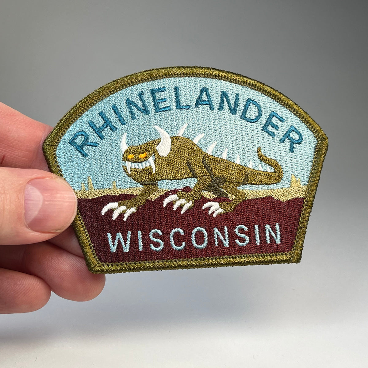 Hand holding the Rhinelander Wisconsin Hodag cryptid travel patch