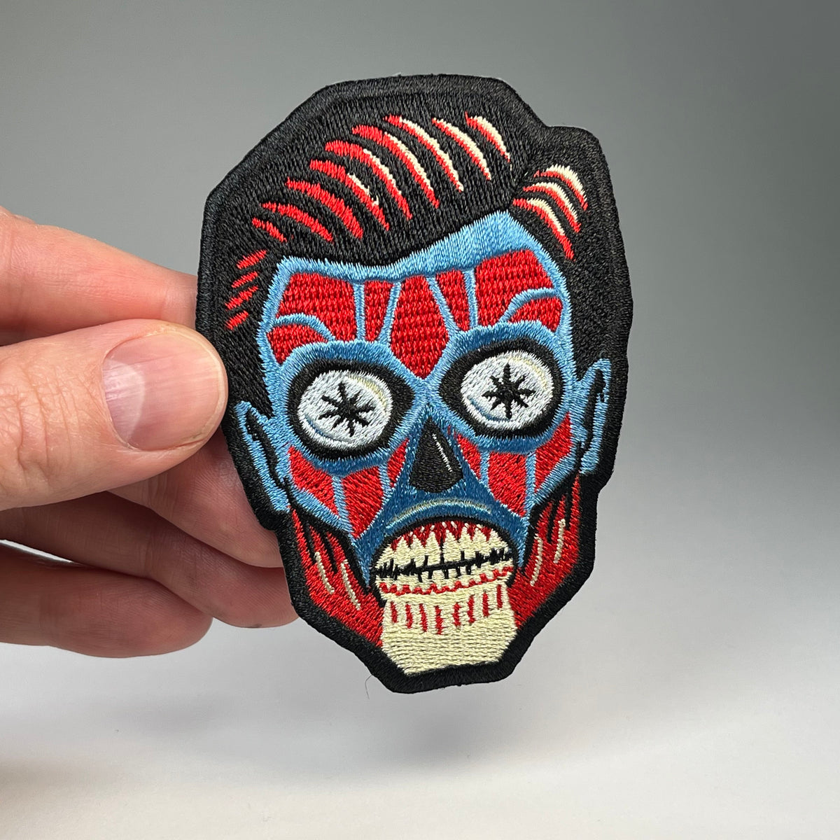 Hand holding the They Live alien head embroidered patch