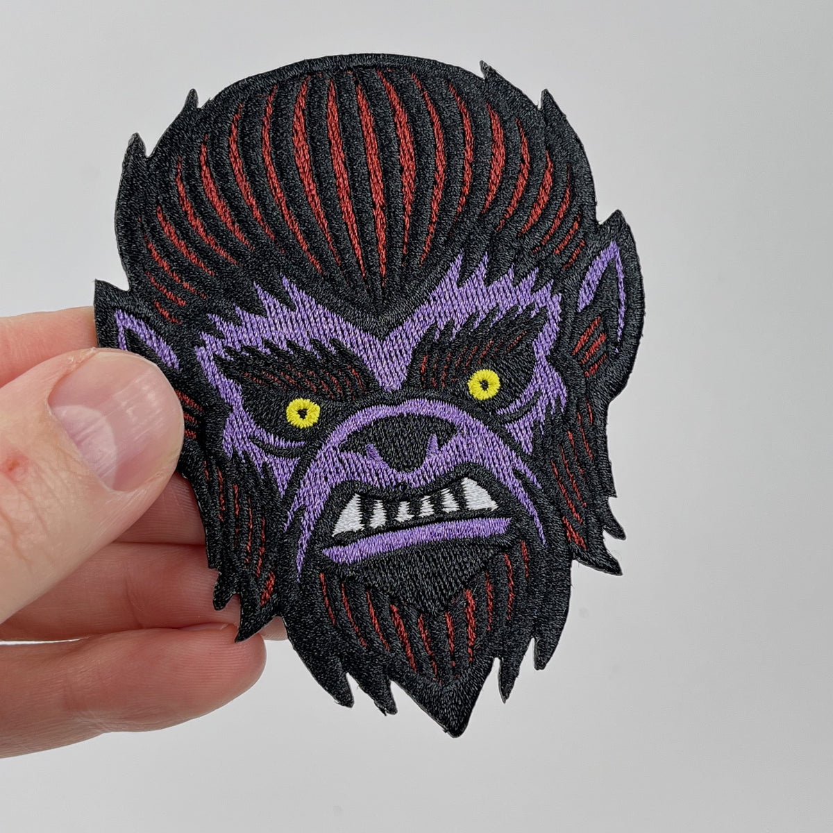 Hand holding the Wolf Man werewolf embroidered patch, snarling purple and red werewolf face