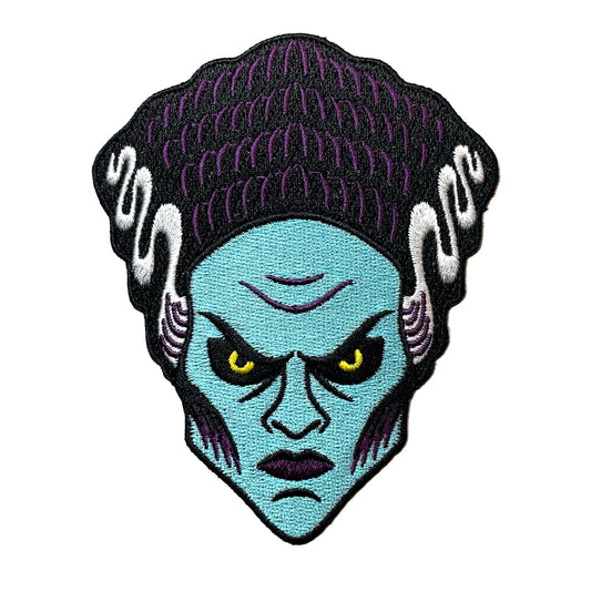 Embroidered patch of a blue-skinned Bride Of Frankenstein with yellow eyes on a white background.